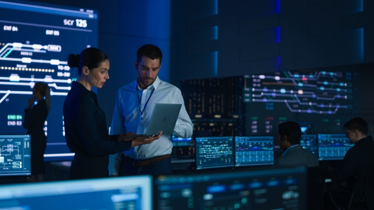 2 people discuss data on a laptop with a screen showing charts and system analysis.